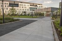 a city street surrounded by grass and tall buildings at the end of a street there is a paved pathway in front of the building