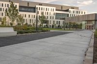 a city street surrounded by grass and tall buildings at the end of a street there is a paved pathway in front of the building