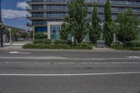 a black paved street with a tall building in the background near some trees and bushes