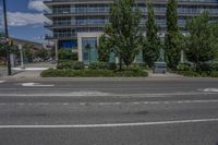 a black paved street with a tall building in the background near some trees and bushes