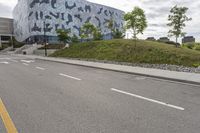 an empty street lined with road markers on a hill in front of a modern building