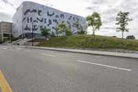 an empty street lined with road markers on a hill in front of a modern building