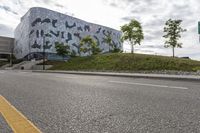 an empty street lined with road markers on a hill in front of a modern building