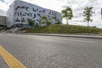 an empty street lined with road markers on a hill in front of a modern building