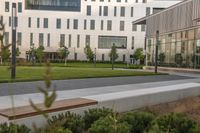 a city street surrounded by grass and tall buildings at the end of a street there is a paved pathway in front of the building