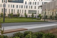 a city street surrounded by grass and tall buildings at the end of a street there is a paved pathway in front of the building