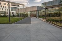 a city street surrounded by grass and tall buildings at the end of a street there is a paved pathway in front of the building