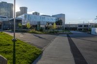 a city street surrounded by grass and tall buildings at the end of a street there is a paved pathway in front of the building