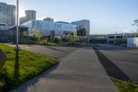 a city street surrounded by grass and tall buildings at the end of a street there is a paved pathway in front of the building