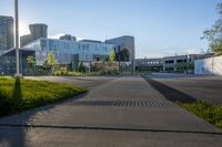 a city street surrounded by grass and tall buildings at the end of a street there is a paved pathway in front of the building