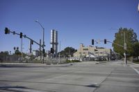 an empty street is near some factory smoke stacks and stop lights with a car coming to the top of it