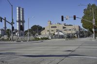 an empty street is near some factory smoke stacks and stop lights with a car coming to the top of it