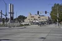 an empty street is near some factory smoke stacks and stop lights with a car coming to the top of it