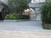 an empty space has a tall planter full of green plants on the ground and a bench with blue benches