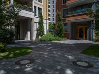 a residential driveway with a bench and bushes in between buildings and green grass on either side