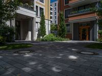 a residential driveway with a bench and bushes in between buildings and green grass on either side