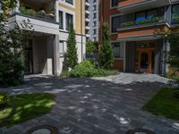 a residential driveway with a bench and bushes in between buildings and green grass on either side