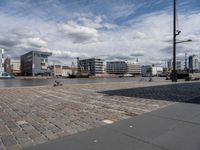 a river has a brick walkway and buildings by it with some boats in the background