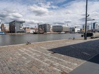 a river has a brick walkway and buildings by it with some boats in the background