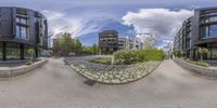 a panorama of buildings, with a bench on the right side of the street, seen through a fish - eye lens