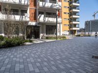 an apartment complex with a building in the background with lots of windows and a brick pathway