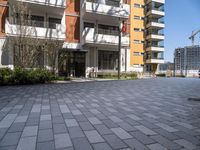 an apartment complex with a building in the background with lots of windows and a brick pathway