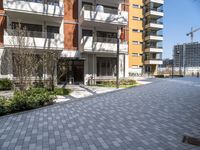 an apartment complex with a building in the background with lots of windows and a brick pathway