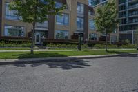 there are two parking meters standing next to each other on the sidewalk, along with a large apartment building and lawn