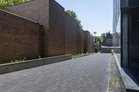 a brick walkway outside a building and two empty benches beside it on the side of a sidewalk