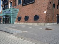 a woman wearing red is walking across the pavement outside her apartment block, which features large circular windows and a brick wall