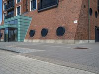 a woman wearing red is walking across the pavement outside her apartment block, which features large circular windows and a brick wall