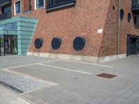 a woman wearing red is walking across the pavement outside her apartment block, which features large circular windows and a brick wall