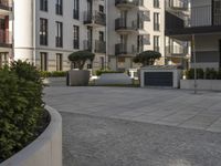 an empty courtyard in front of buildings and some bushes on the ground with some trees in the middle