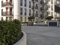 an empty courtyard in front of buildings and some bushes on the ground with some trees in the middle