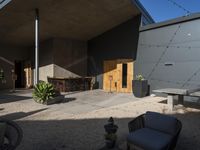 a chair sitting on top of a gravel floor next to a table and benches next to trees