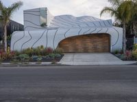 the modern home has a curved design on its facade and features a garage with lots of potted plants