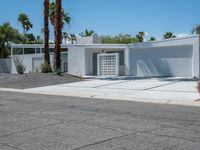 a white building with multiple windows sitting on the side of a road next to two palm trees