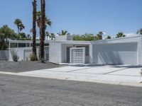 a white building with multiple windows sitting on the side of a road next to two palm trees