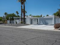 a white building with multiple windows sitting on the side of a road next to two palm trees