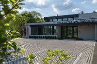 a parking lot near the building with windows and bushes in front of it and a tree outside