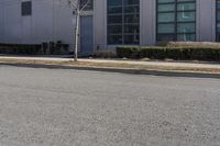 a person is on a skate board in the street on a clear day with buildings and green bushes