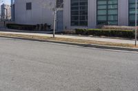 a person is on a skate board in the street on a clear day with buildings and green bushes