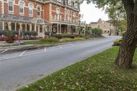 a large red brick building sits next to a tree near the street and lawn of some homes