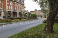 a large red brick building sits next to a tree near the street and lawn of some homes