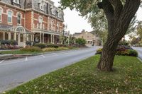 a large red brick building sits next to a tree near the street and lawn of some homes