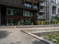 a concrete plaza near apartment buildings with many plants growing in the area behind it,