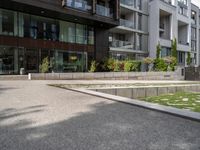 a concrete plaza near apartment buildings with many plants growing in the area behind it,