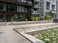 a concrete plaza near apartment buildings with many plants growing in the area behind it,