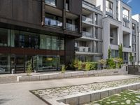 a concrete plaza near apartment buildings with many plants growing in the area behind it,