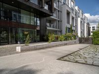 a concrete plaza near apartment buildings with many plants growing in the area behind it,